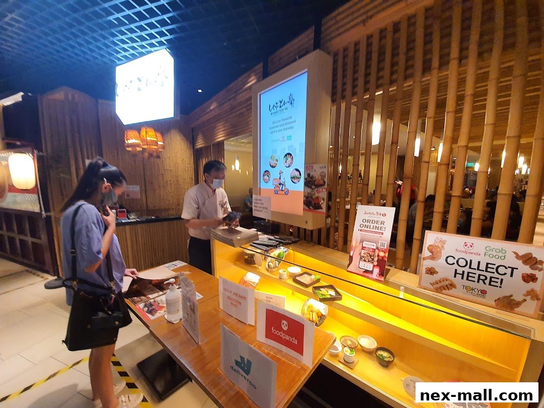 A customer is ordering at a Japanese food counter with food displays and delivery service signs.