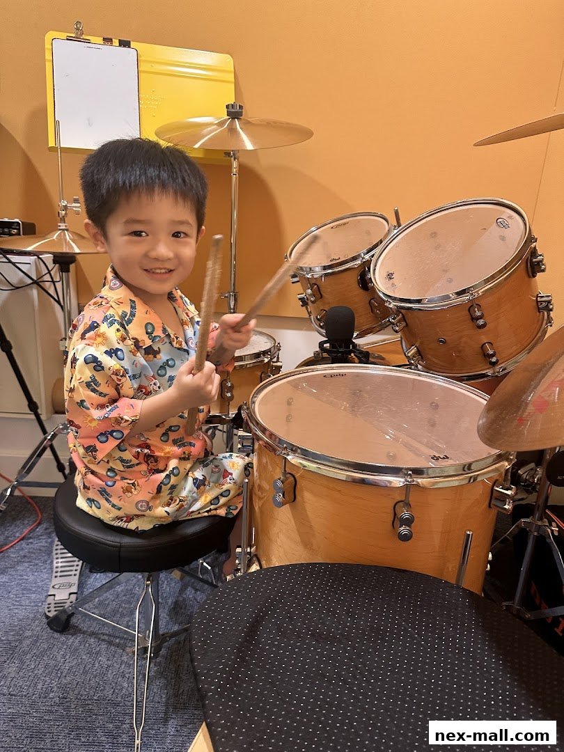 A young boy smiles while sitting at a drum set, holding drumsticks.