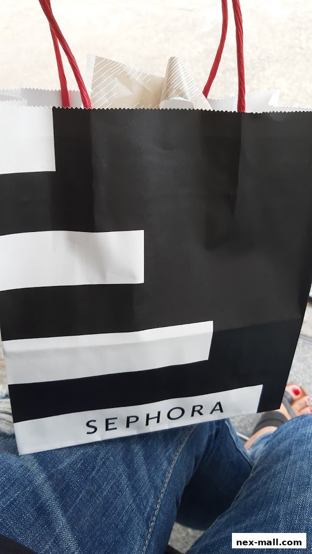 A black and white Sephora shopping bag with red handles held by a person in jeans.