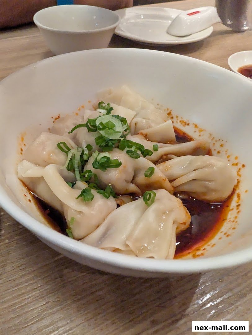 A bowl of delicious wontons in chili oil, garnished with green onions.