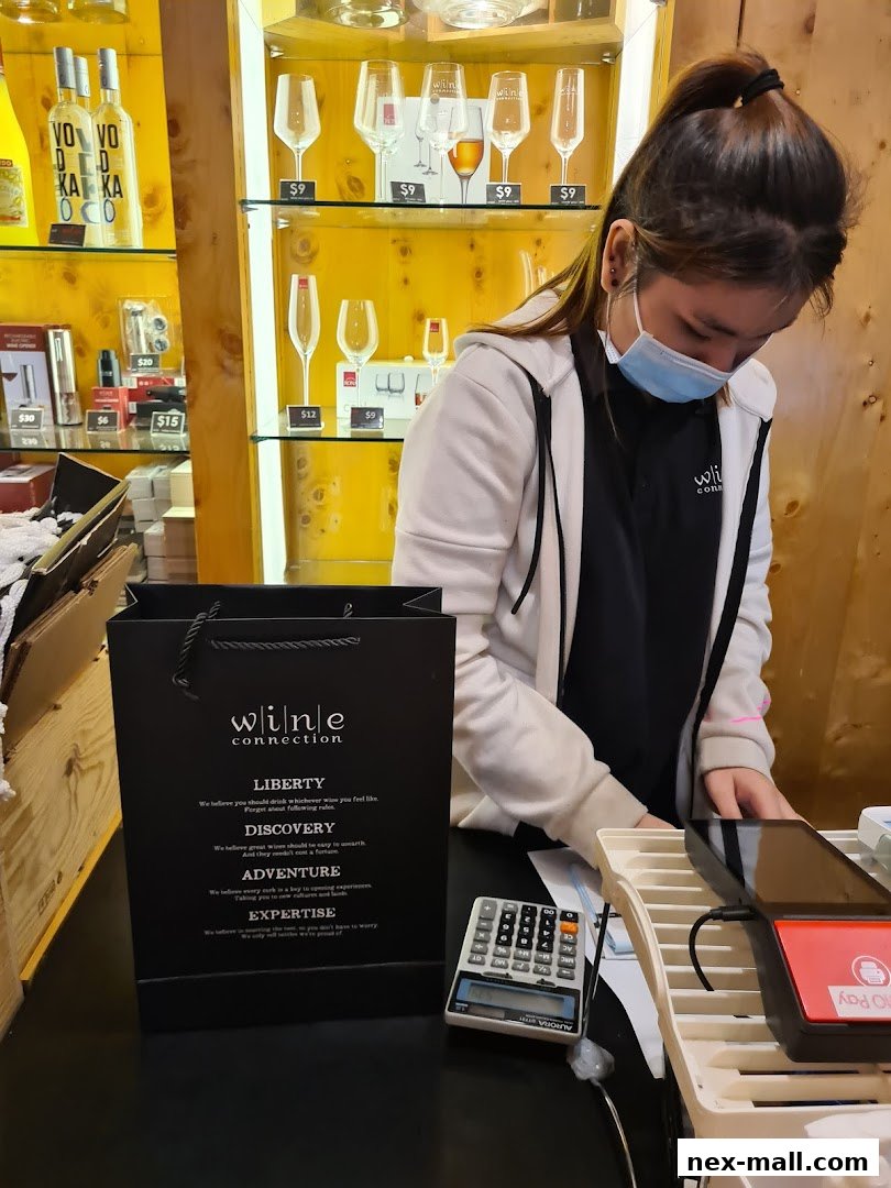 A staff member at Wine Connection NEX is seen at the counter with a shopping bag and calculator.
