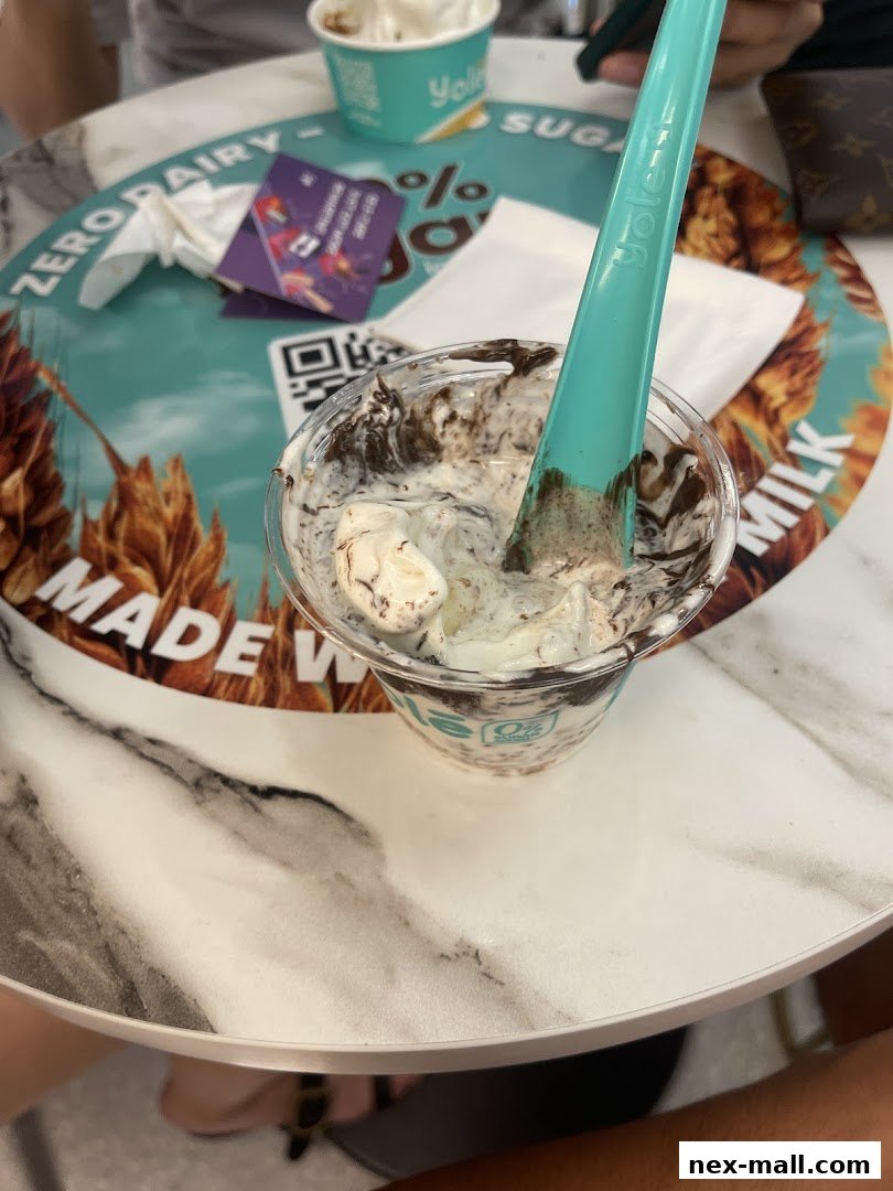 A cup of frozen yogurt with chocolate chunks and a teal spoon on a table.
