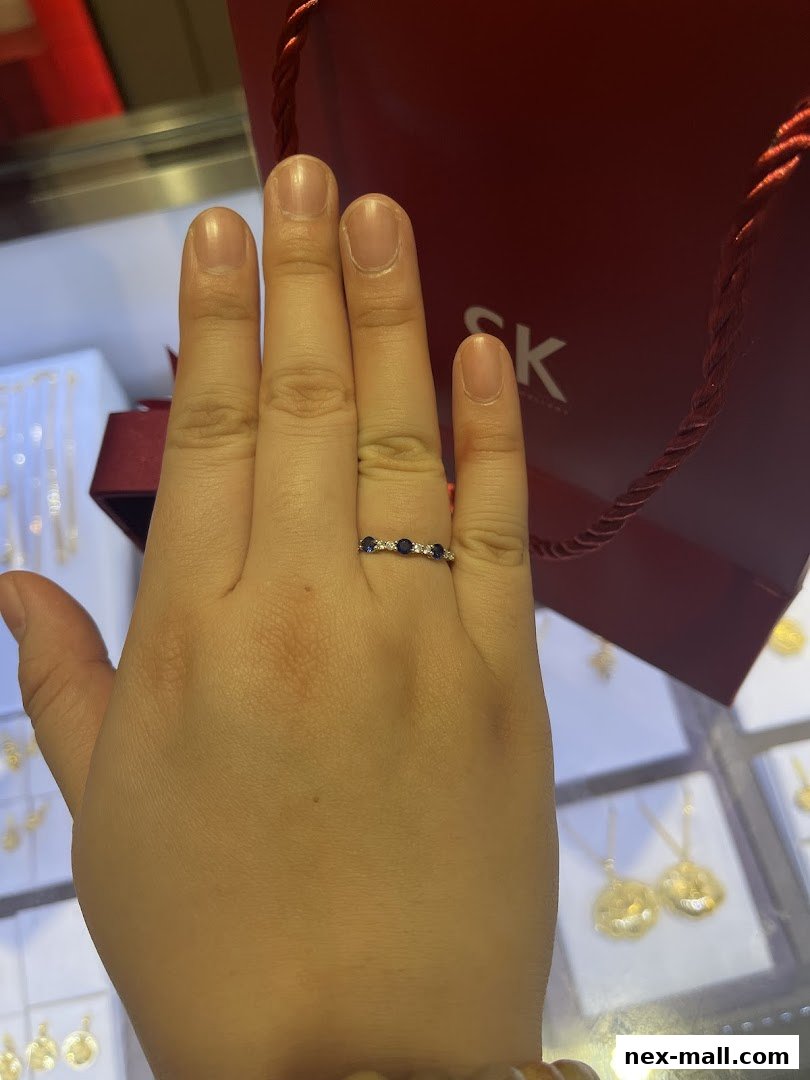 A hand wearing a sapphire and diamond ring in front of a red SK Jewellery bag.