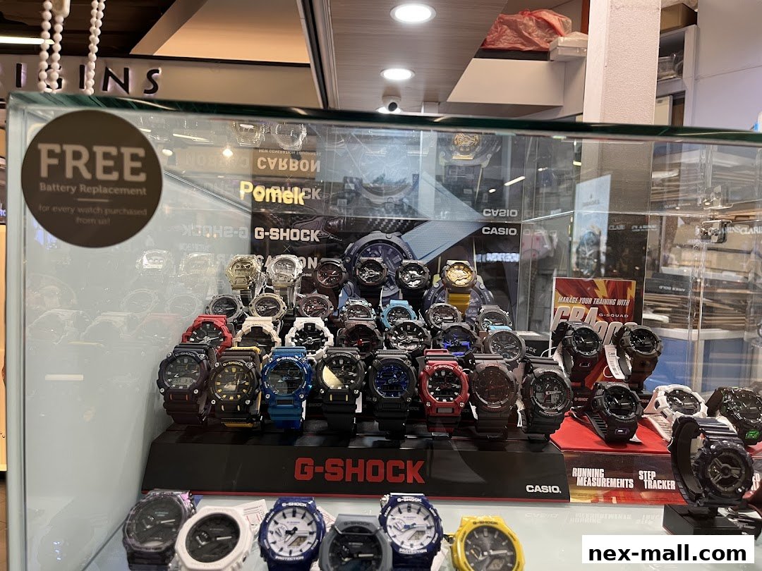A display case filled with various G-Shock watches, featuring a 'Free Battery Replacement' sign.
