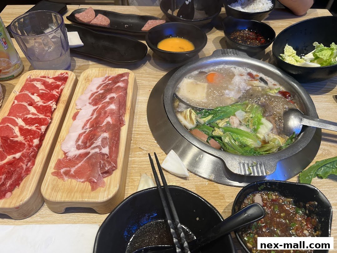 A table laden with a hot pot, thinly sliced meats, dipping sauces, and a drink.
