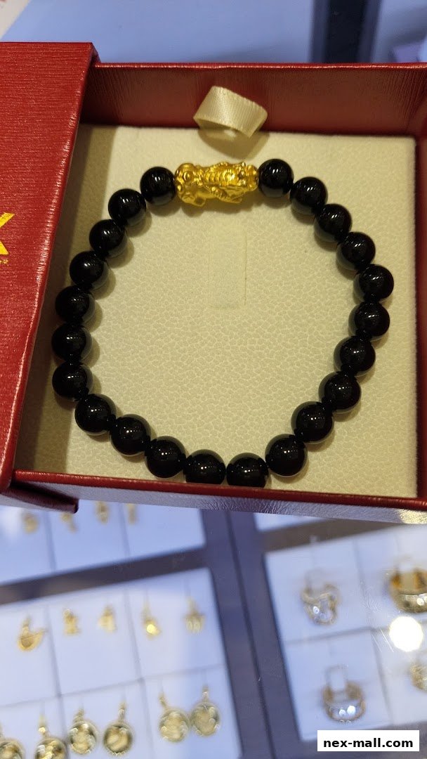 A close-up of a black beaded bracelet with a gold Pixiu charm in a red jewelry box.
