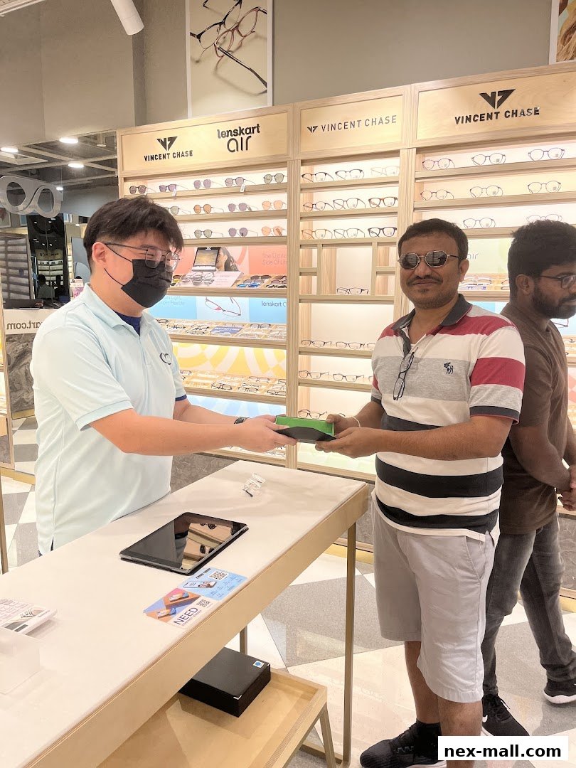 A store employee hands a customer a pair of glasses at Lenskart NEX.