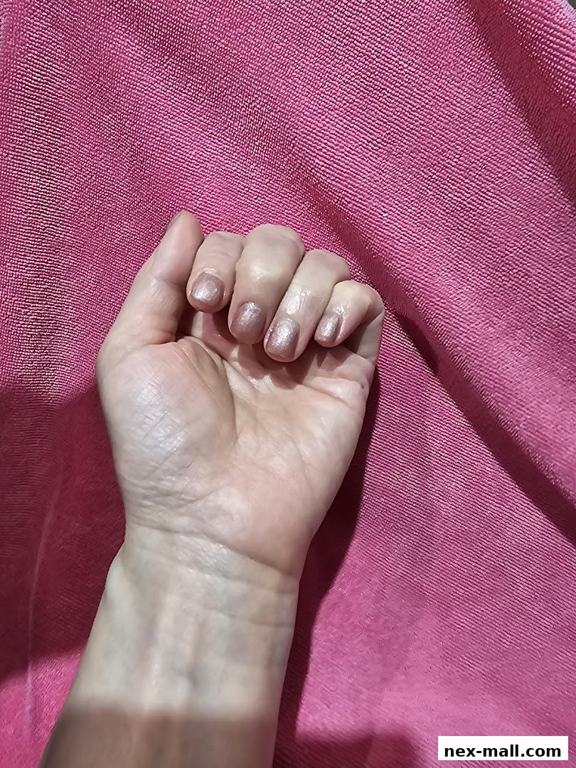 A hand with light pink glitter nail polish against a textured pink background.