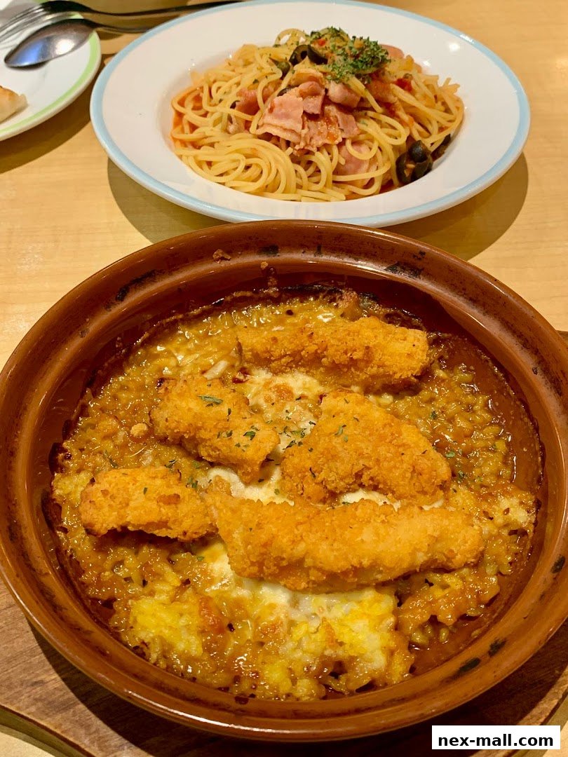 A close-up of two delicious dishes: a baked rice dish with fried chicken and cheese, and a spaghetti dish with bacon and olives.