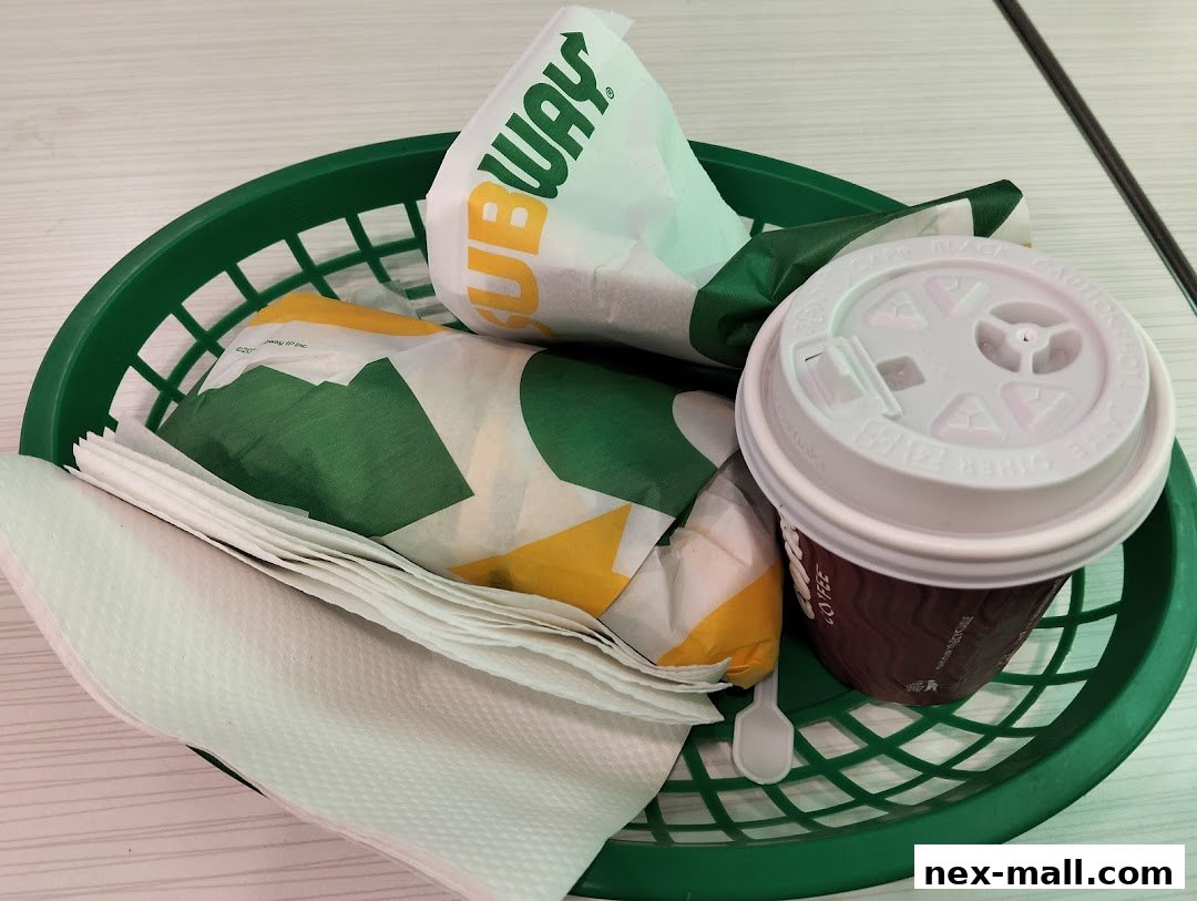 A green basket filled with Subway sandwiches, napkins, and a coffee cup.