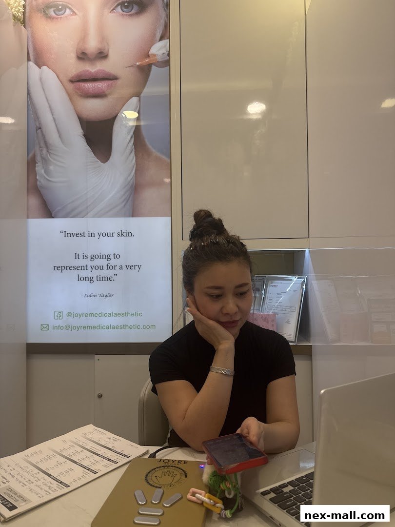 A woman sits at a desk in a spa, with a poster about skincare behind her.