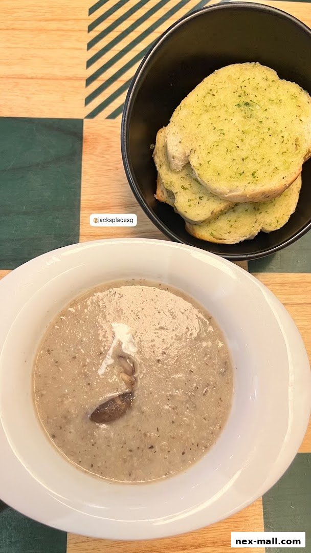 A bowl of creamy mushroom soup with a slice of mushroom and garlic bread.