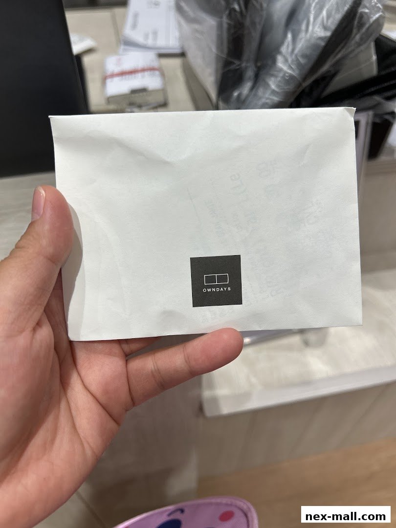A hand holds a white paper with the OWNDAYS logo on it.