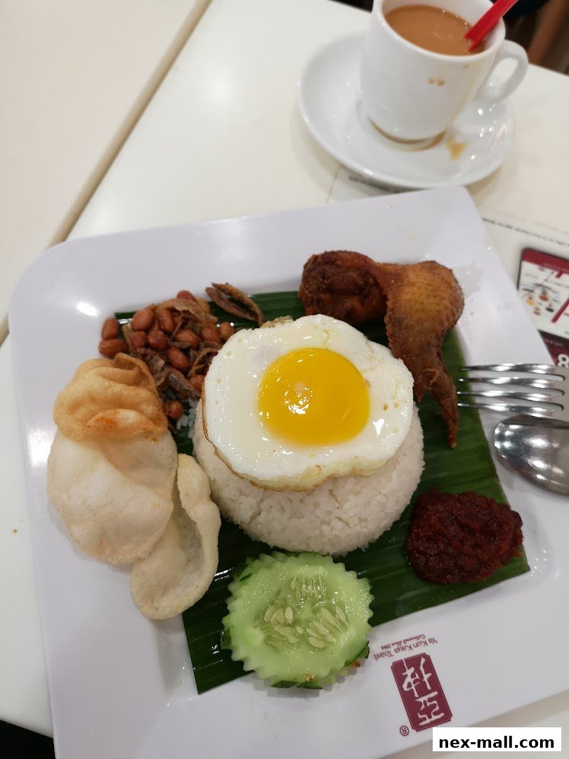 A plate of Nasi Lemak with fried chicken, egg, peanuts, anchovies, cucumber, and sambal, served with coffee.