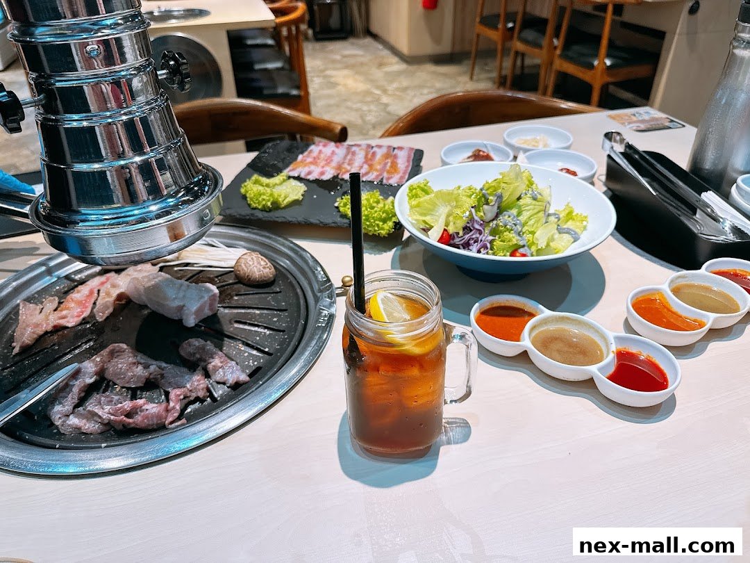 A table set for Korean BBQ with raw meat, salad, dipping sauces, and iced tea.