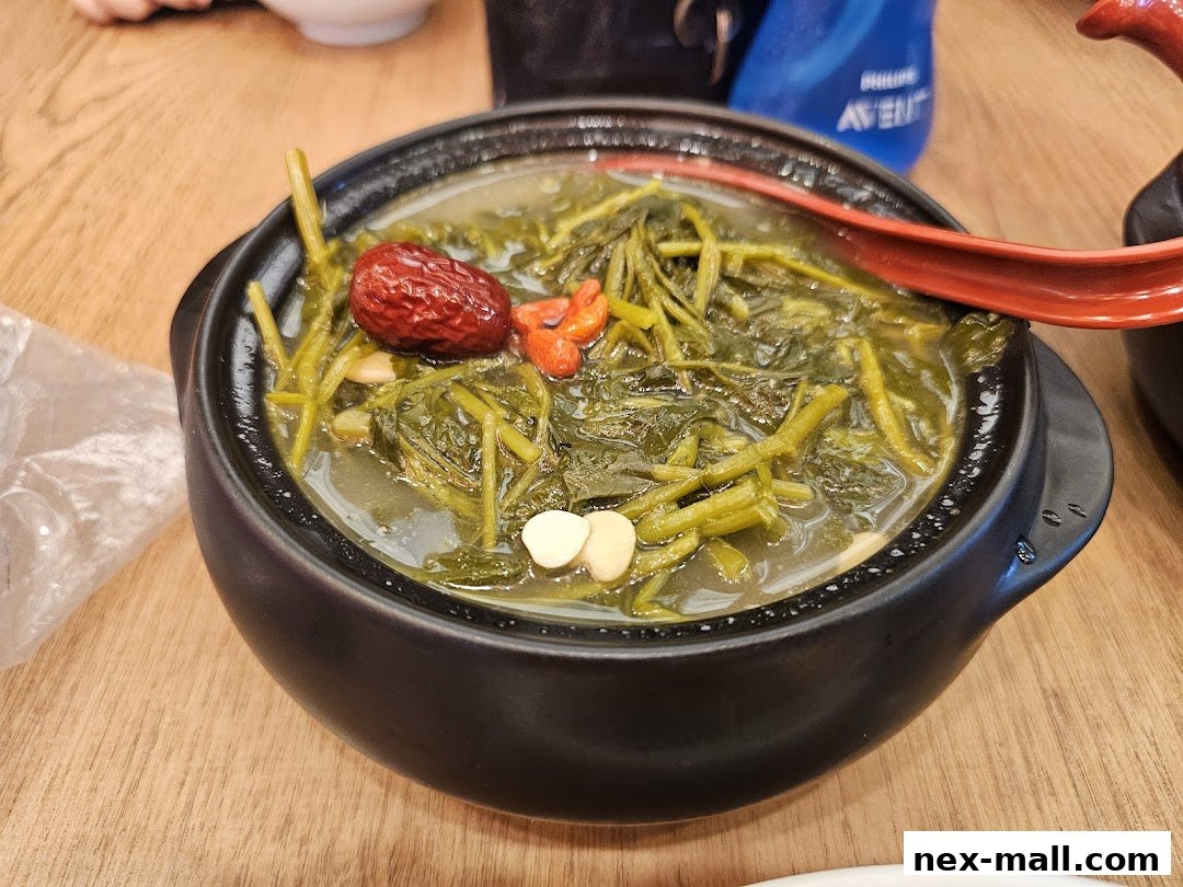 A close-up of a steaming bowl of herbal soup with vegetables and red dates.