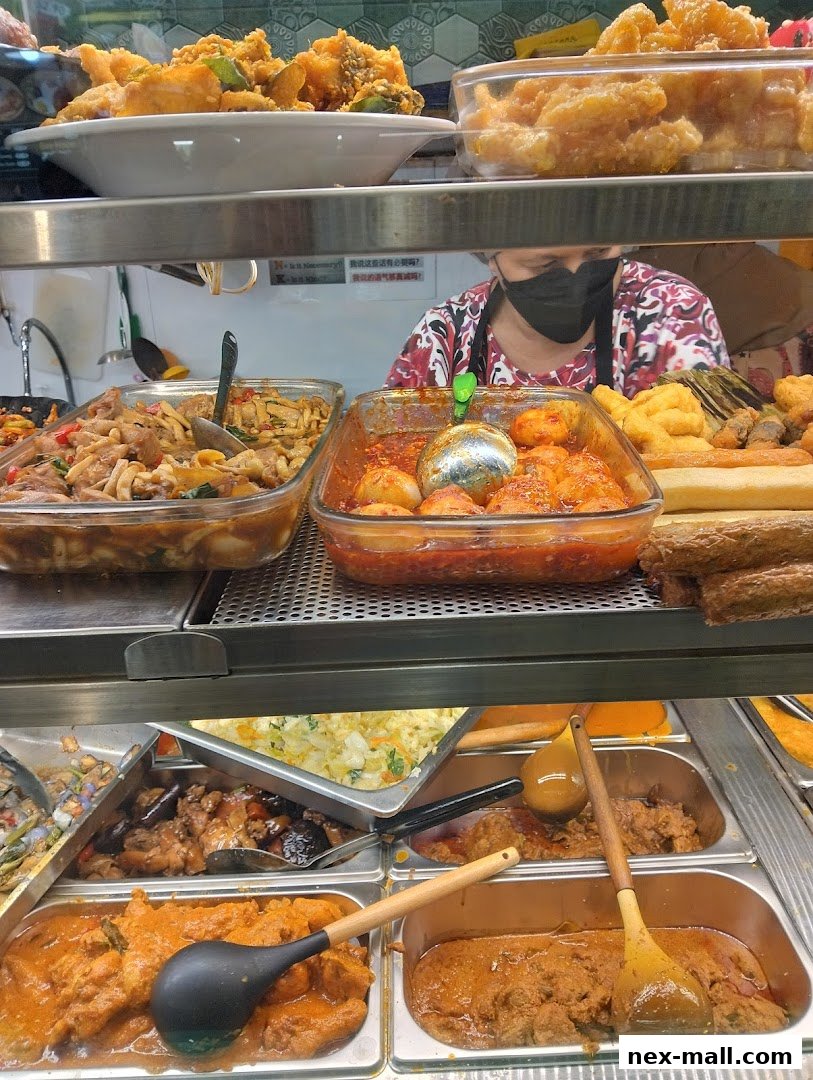 A display of various cooked dishes in metal trays, with a person in the background.