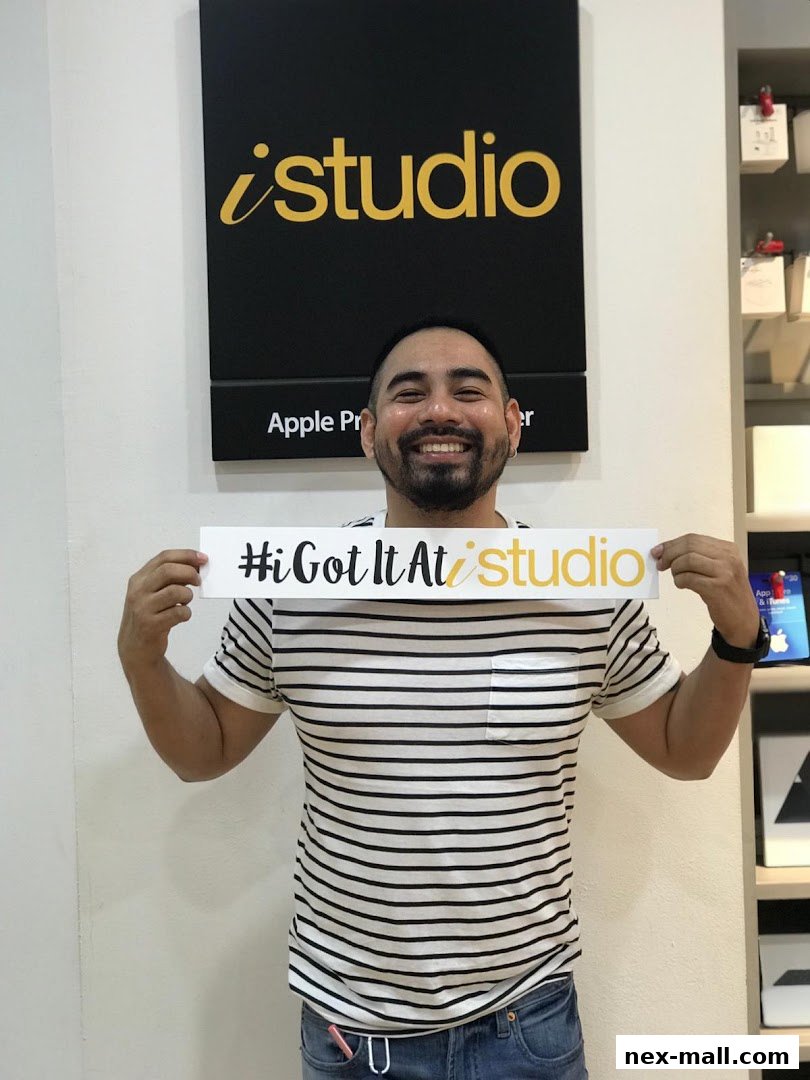 A smiling man holds a sign that says '#iGotItAt studio' in front of an iStudio store.