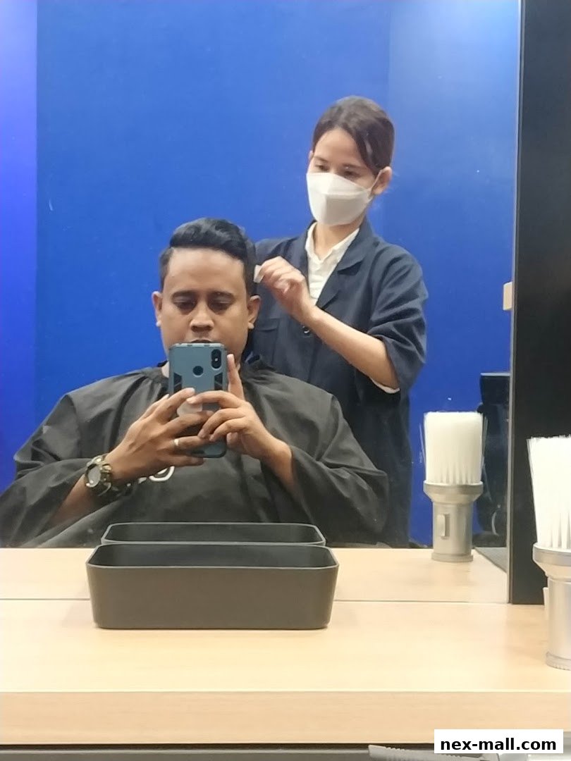 A barber is cutting a man's hair in a salon, reflected in a mirror.