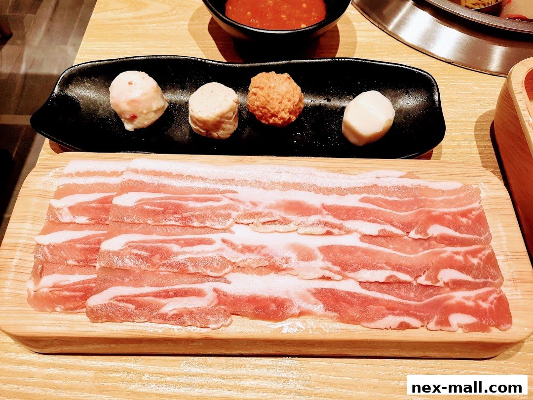 A close-up of thinly sliced pork belly and assorted meatballs on a black plate.