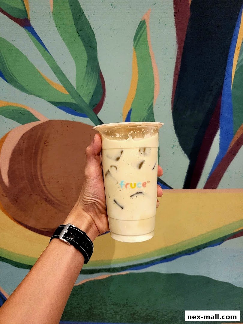 A hand holds a creamy beverage with ice and the Fruce logo against a colorful abstract background.