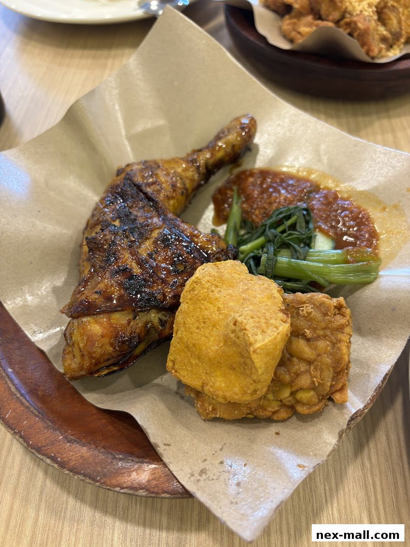 A close-up of a delicious Ayam Penyet dish with grilled chicken, tofu, tempeh, and vegetables.