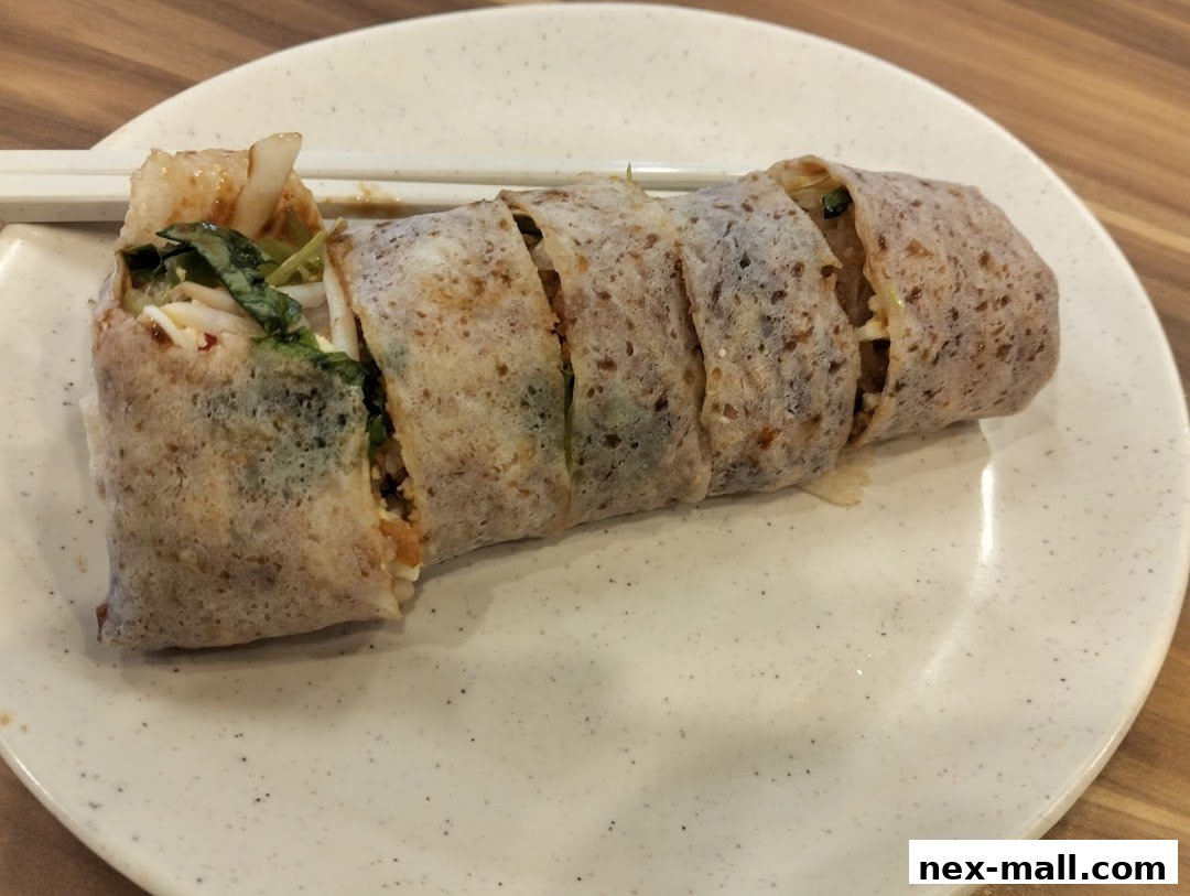 A sliced popiah roll filled with vegetables and other ingredients on a speckled white plate.