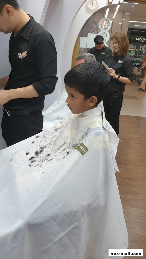A young boy sits in a barber's chair, draped in a cape, as a stylist prepares to cut his hair.