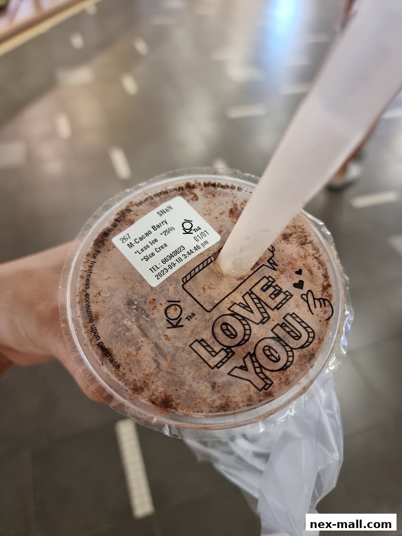 A hand holds a KOI Thé drink with a straw, showing the lid with order details and a 'Love You' message.