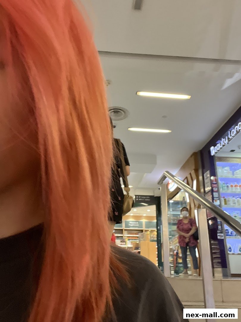 A person with bright pink hair is in the foreground, with a shop interior visible in the background.