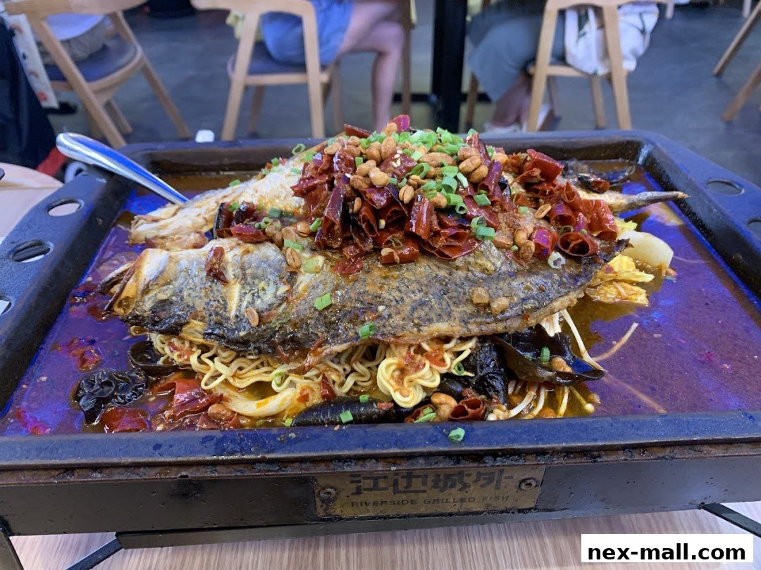 A close-up of a grilled fish dish with noodles, chili peppers, and peanuts.