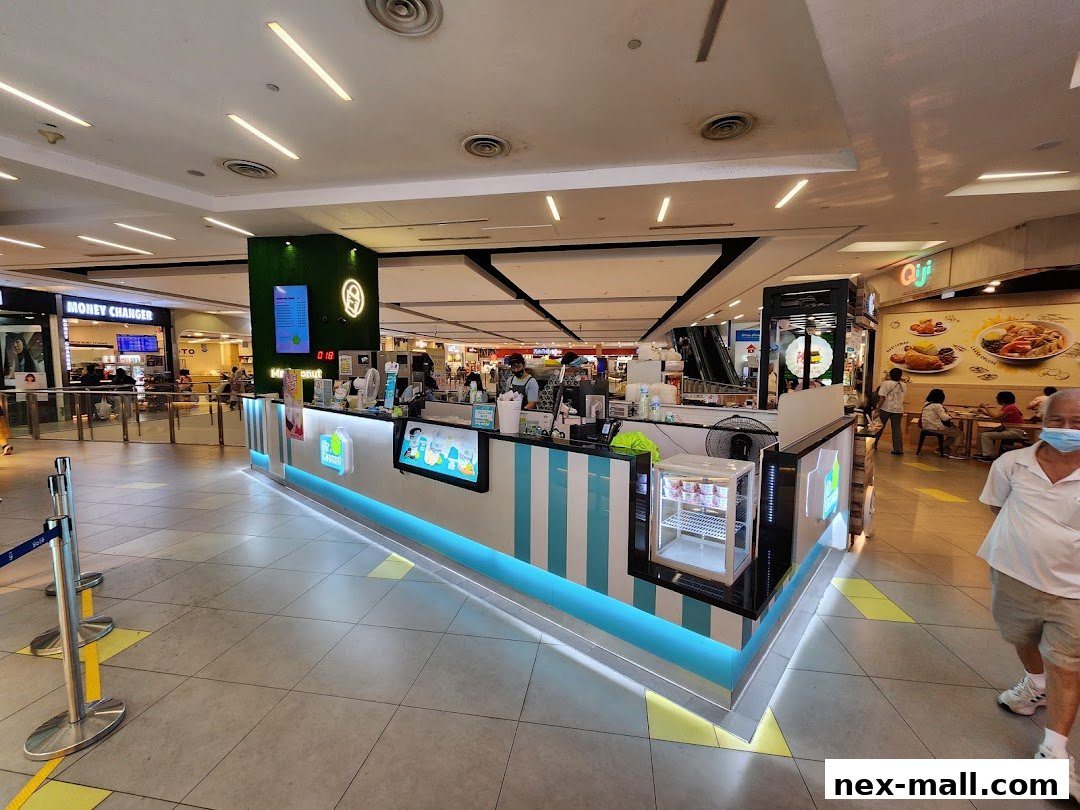 A brightly lit Mr. Coconut NEX kiosk in a shopping mall with customers and other shops visible.