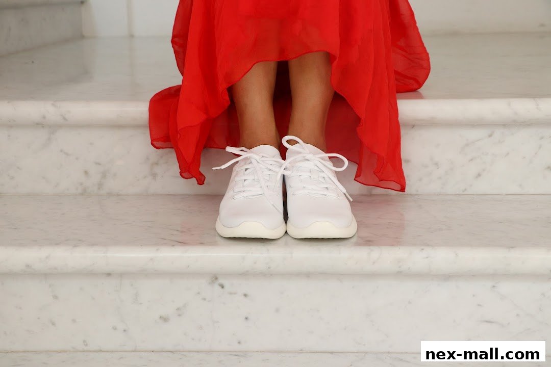 A person wearing white sneakers and a red dress stands on marble stairs.