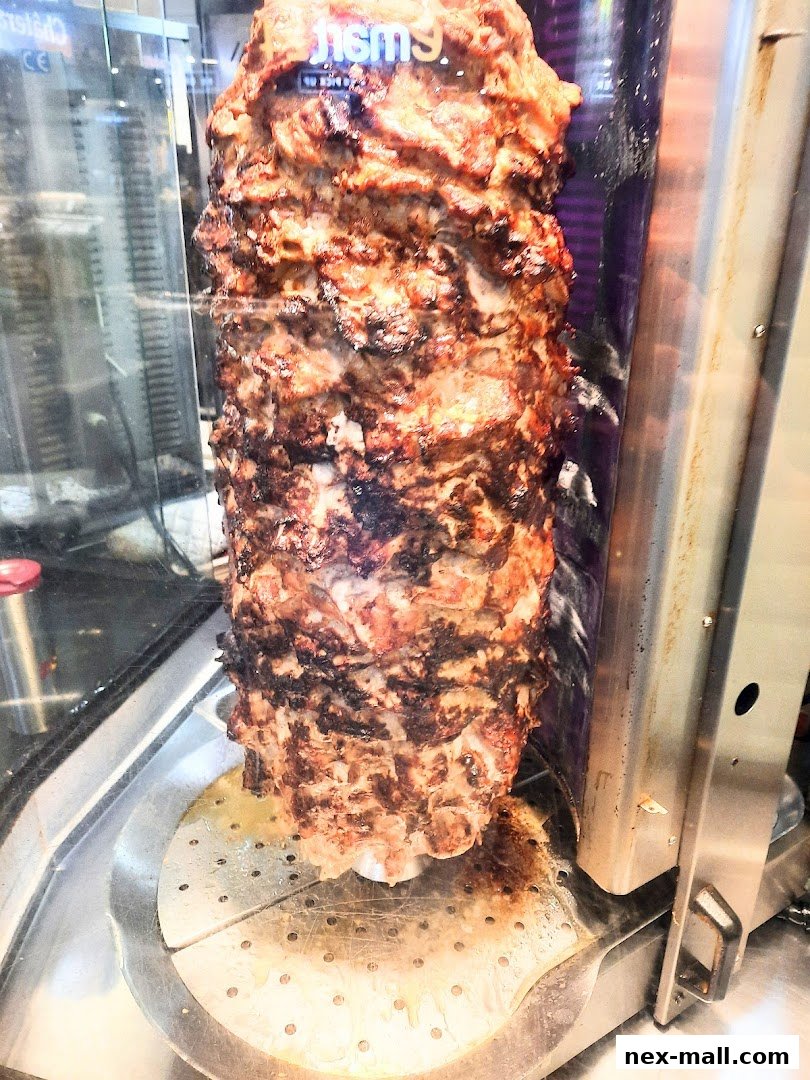 A vertical rotisserie grill with seasoned meat cooking.