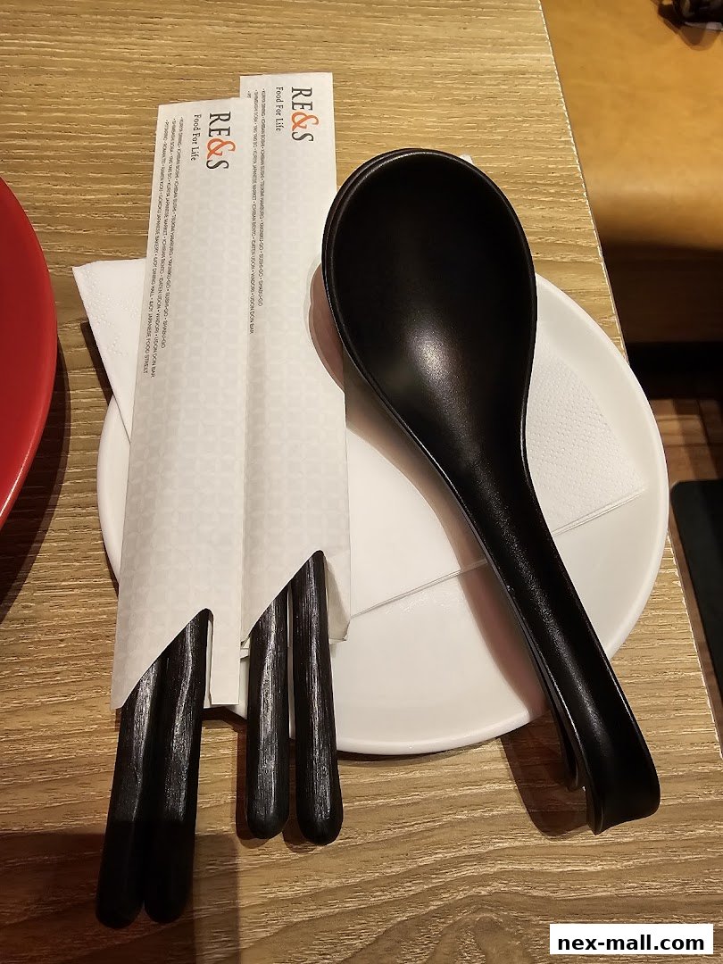 A black spoon and chopsticks are placed on a white plate with a napkin.