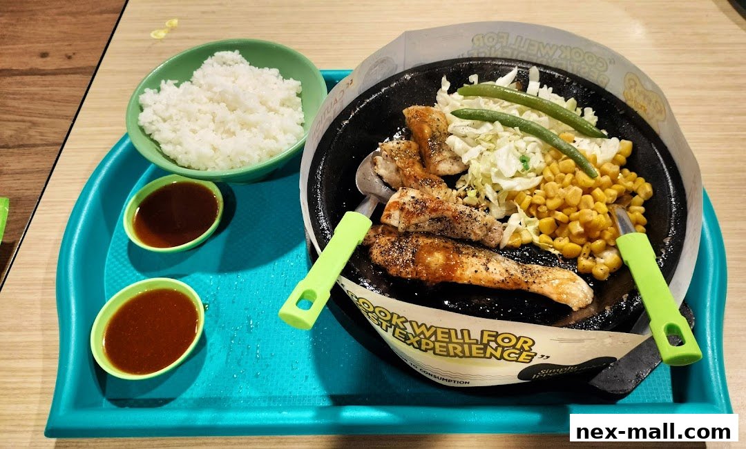 A sizzling hot plate meal with chicken, corn, cabbage, and green beans, served with rice and sauce.