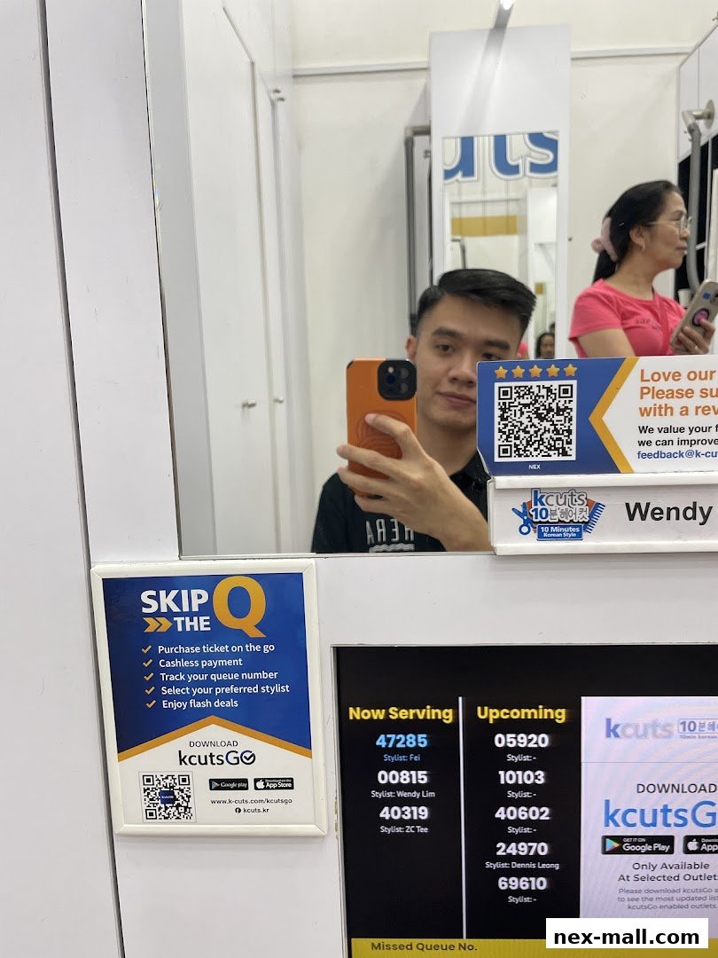 A man takes a selfie in a salon mirror, showing a queue display and promotional material.