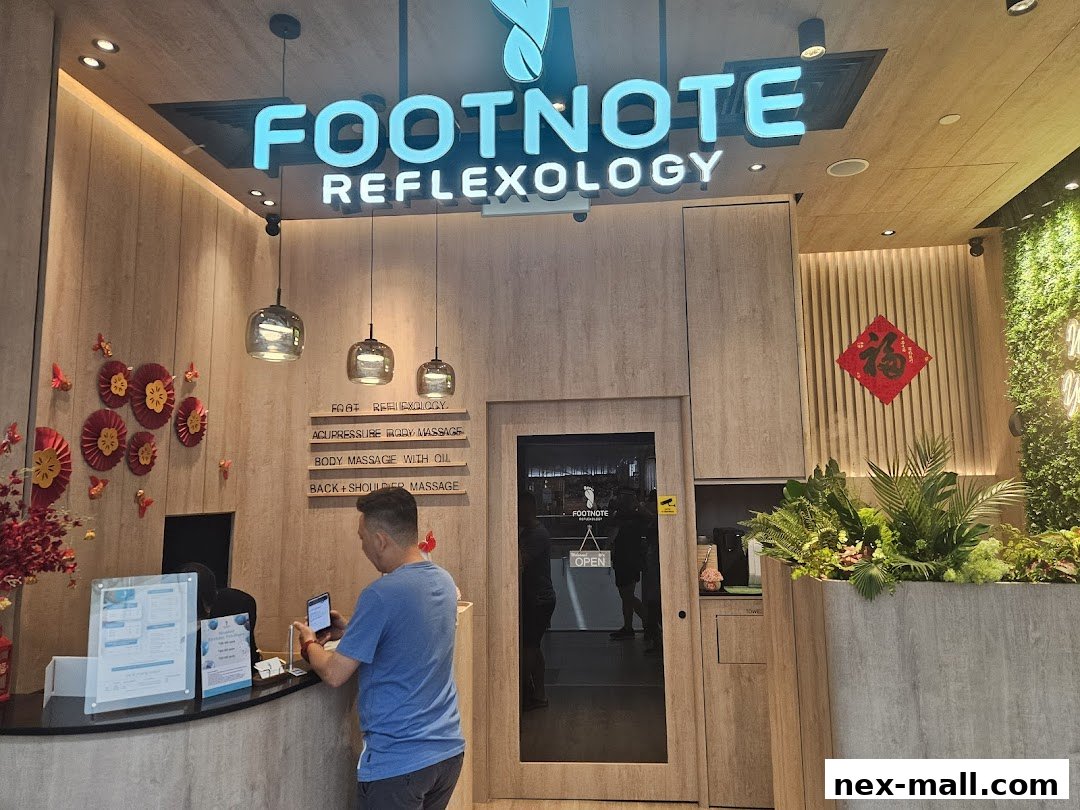 The entrance of FootNote Reflexology with its illuminated sign and a customer at the counter.