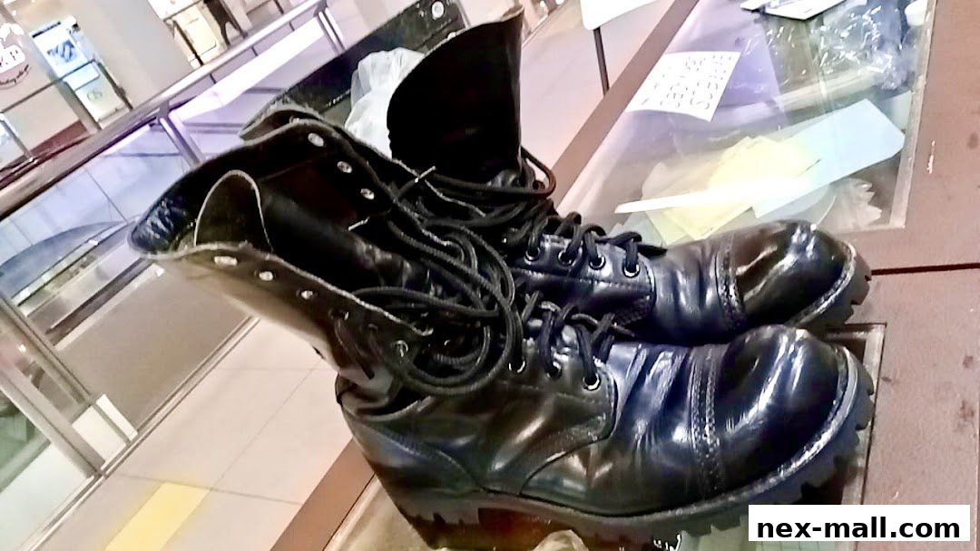 A pair of shiny black lace-up boots are displayed on a glass surface.