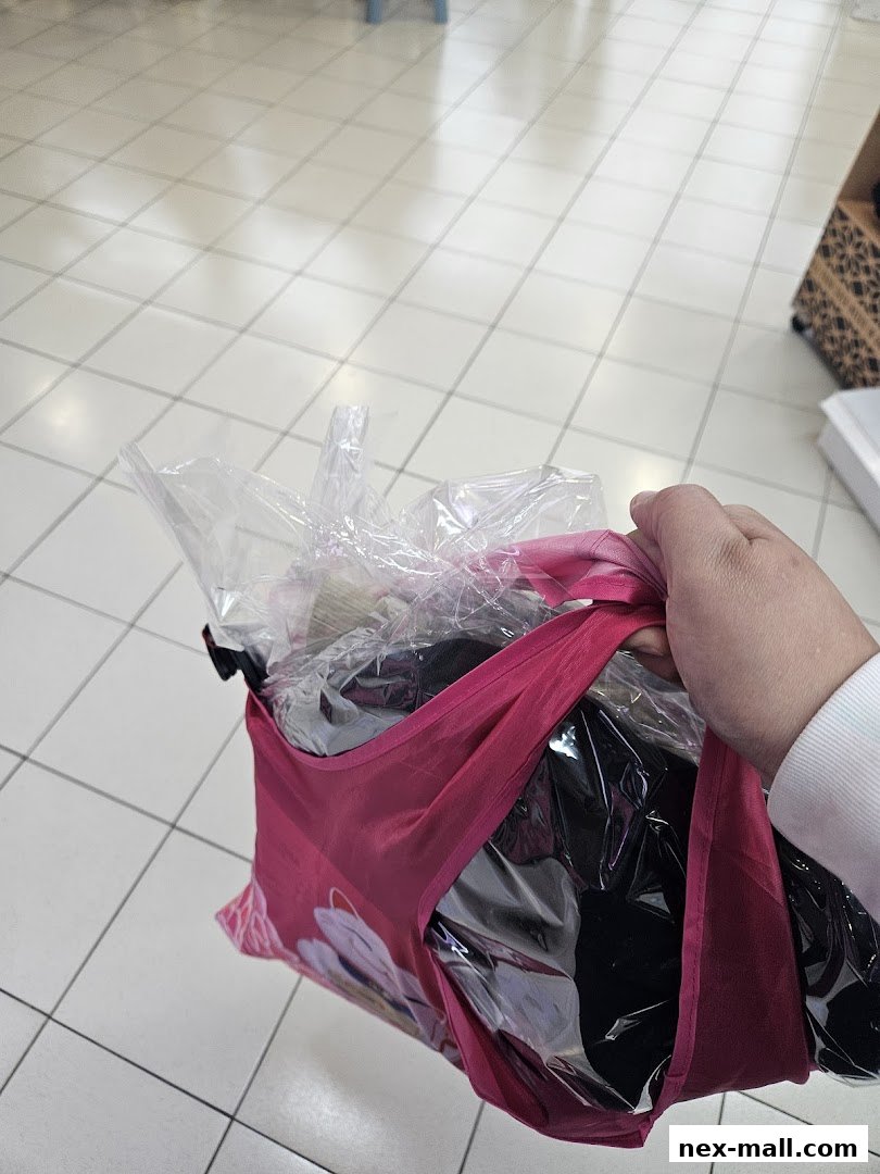 A hand holds a pink reusable bag filled with clothes in plastic packaging.