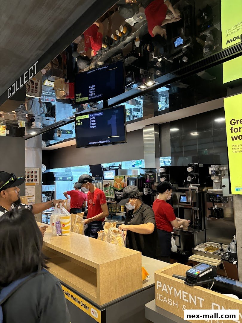 McDonald's staff serving customers at the counter with digital order screens visible.