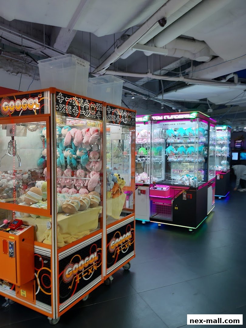 Several colorful claw machines filled with plush toys are lined up in a brightly lit arcade.