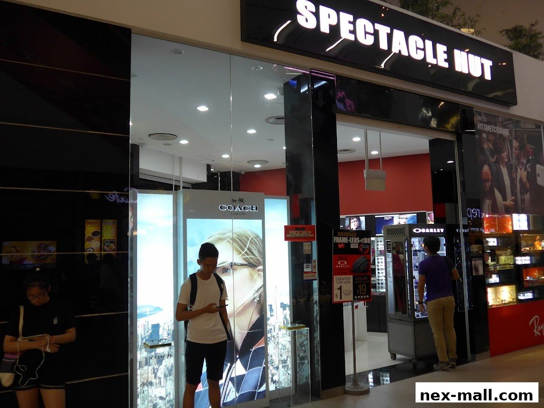 Spectacle Hut NEX shop front with displays of eyewear and a Coach advertisement.