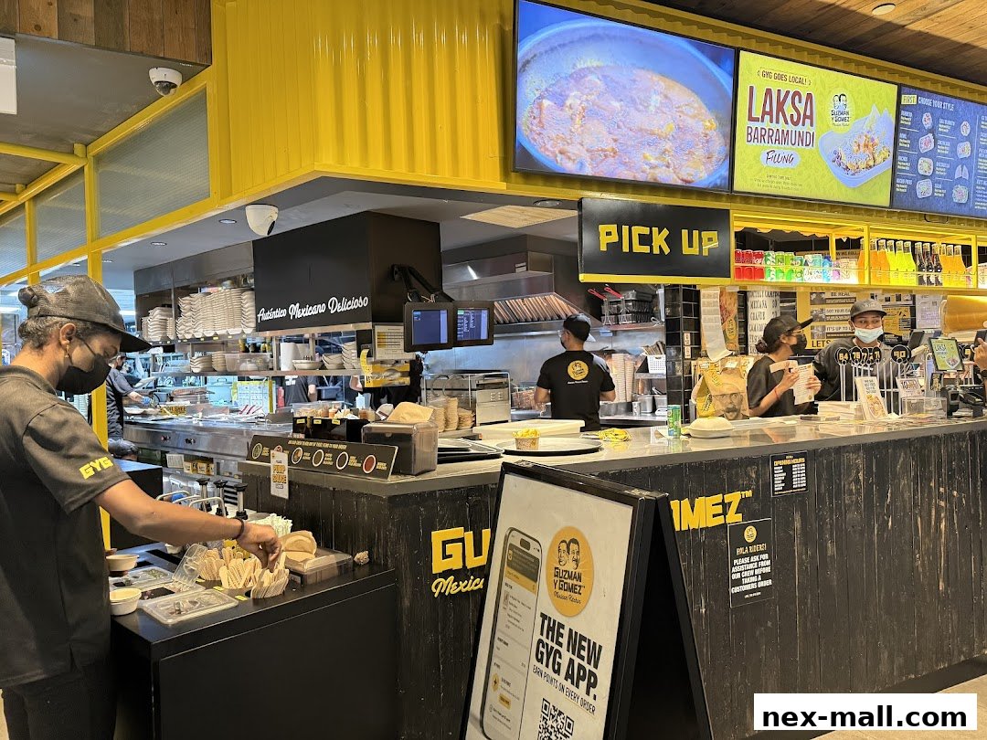 Staff preparing food behind the counter at Guzman y Gomez, with a pick-up sign and menu boards visible.