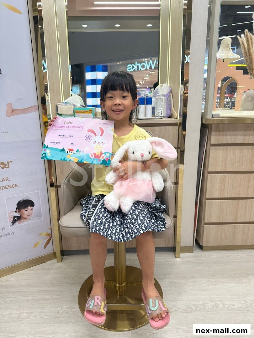 A smiling young girl holds a piercing certificate and a stuffed bunny in a jewelry shop.
