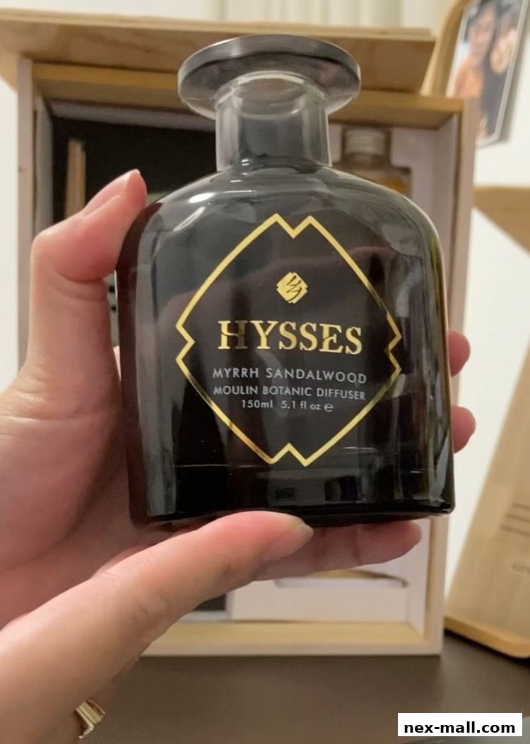 A hand holds a black glass diffuser bottle with a gold label.