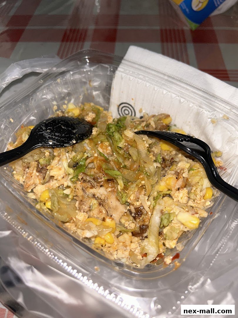 A close-up of a takeout container filled with a rice bowl, featuring chicken, corn, and lettuce.