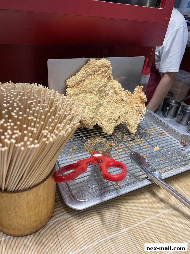 A large, crispy fried chicken cutlet is displayed with chopsticks, scissors, and tongs.