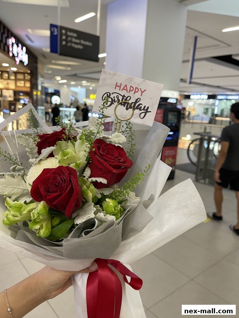 A hand holds a bouquet of red roses and greenery with a 'Happy Birthday' card.
