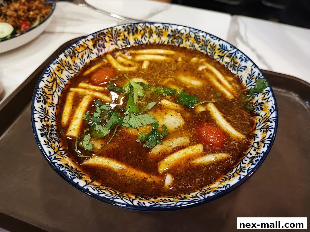 A close-up of a steaming bowl of noodles with broth, cherry tomatoes, and cilantro.